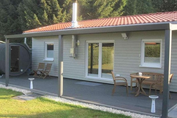 Ein Haus mit überdachter Terrasse, Grill und Gartenmöbeln.
