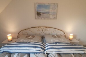 A bed with striped bedding and pillows, a decorative wall piece, and two bedside lamps. - Holiday apartment with 2 bedrooms (Borkum)
