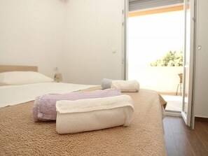 A bedroom with a bed, two rolled towels, a nightstand, and a sliding glass door leading to an outdoor area. - Pansion Jurko - Superior Double Room With Balcony and Sea View (Pag)
