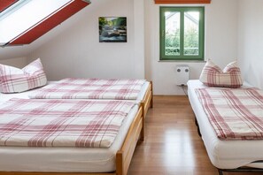 Een kamer met twee bedden, een dakraam, een raam en een schilderij aan de muur.