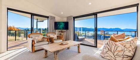 Amplia sala de estar con un gran ventanal, televisor de pantalla plana y balcón con vistas a las montañas.