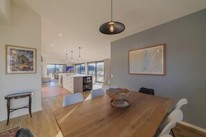 Un comedor amplio con una mesa de madera, sillas blancas y un centro de mesa tejido.