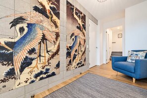 A modern interior with a blue sofa, a large wall mural of birds, and a hallway leading to another room. - The Lookout | Tekapo Lake Views | Sleeps 6 (Lake Tekapo)