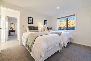 A bedroom with two beds, a window with a view of a rocky landscape, and a door leading to another room. - The Lookout | Tekapo Lake Views | Sleeps 6 (Lake Tekapo)