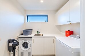 A laundry room with a washing machine, dryer, and a window above the sink. - The Lookout | Tekapo Lake Views | Sleeps 6 (Lake Tekapo)