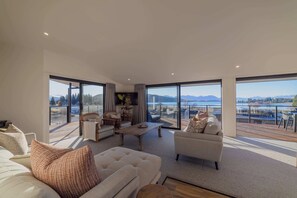 Amplia sala de estar con ventanas grandes, un sofá, una mesa de centro y vistas a un lago y montañas.