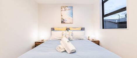 Una cama bien hecha con una colcha azul, dos lámparas de noche y un cuadro sobre la cama.