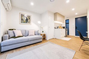 A modern living room with a sofa, a dining area with a chair, and a kitchen with cabinets and appliances. - Modern 2BR with Patio | Christchurch CBD (Christchurch)