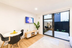 A modern interior with a dining area, a TV mounted on the wall, and a sliding glass door leading to an outdoor space. - Modern 2BR with Patio | Christchurch CBD (Christchurch)