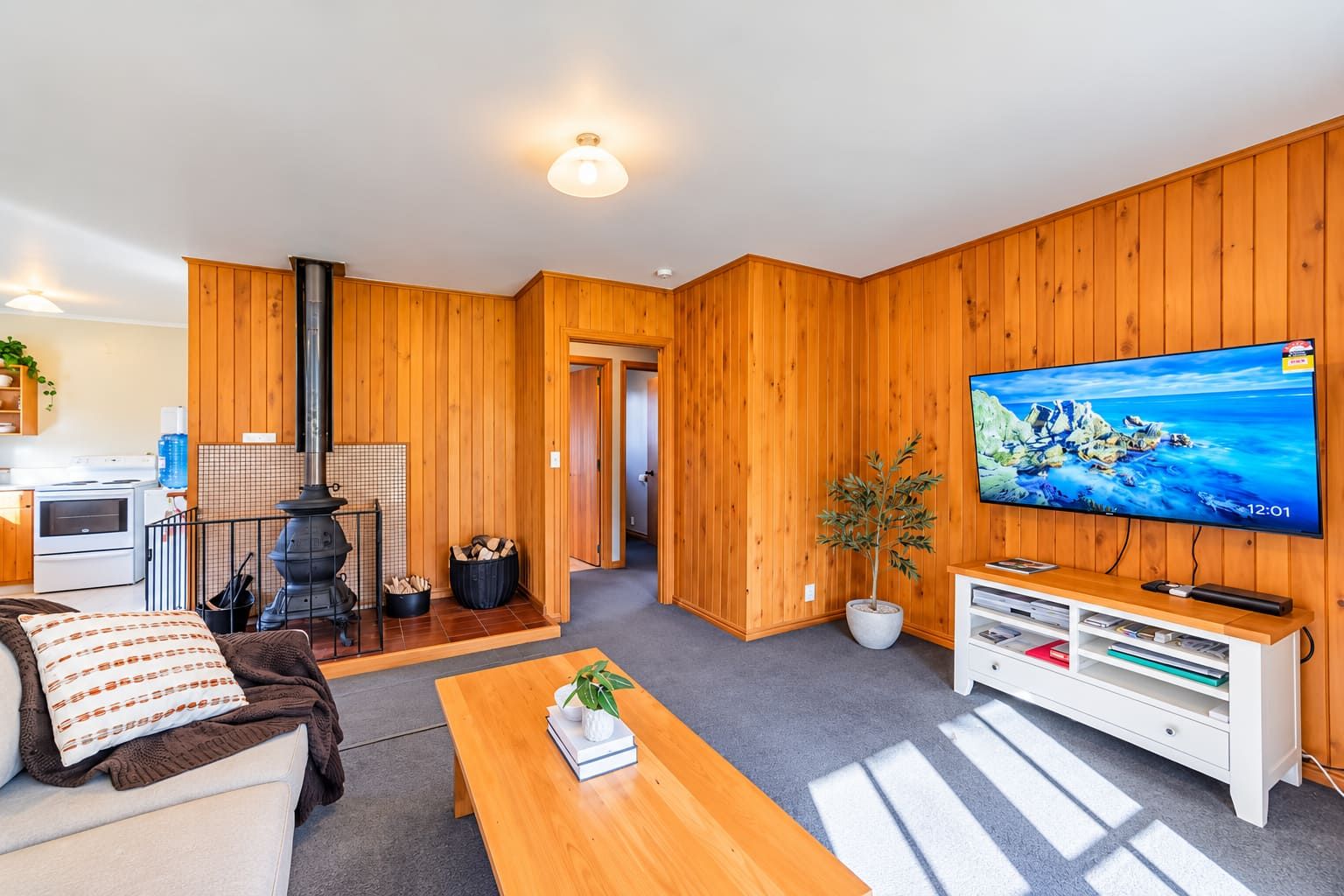 Una sala de estar moderna con detalles de madera, un televisor, una chimenea y una zona de cocina.