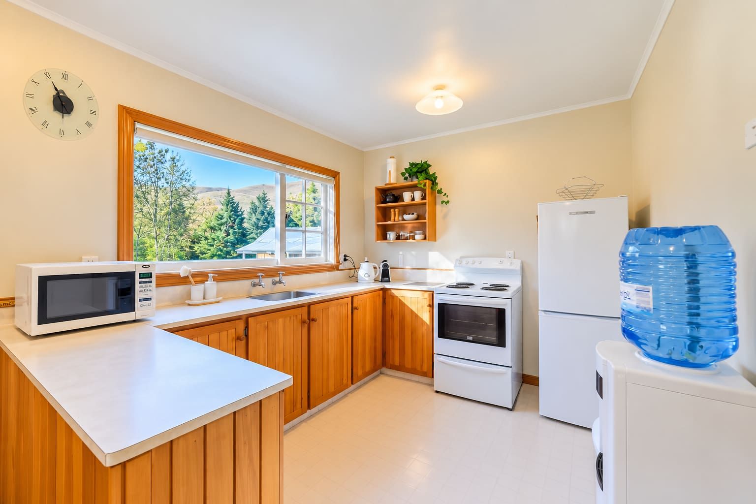 A compact kitchen with wooden cabinets, a microwave, a stove, a sink, and a refrigerator.
