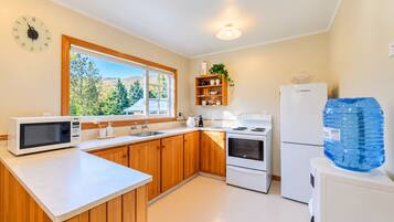 A compact kitchen with wooden cabinets, a microwave, a stove, a sink, and a refrigerator.