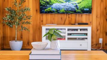 Una mesa de madera con una planta y un cuenco encima de un libro, un televisor en la pared y un mueble blanco para equipos electrónicos.
