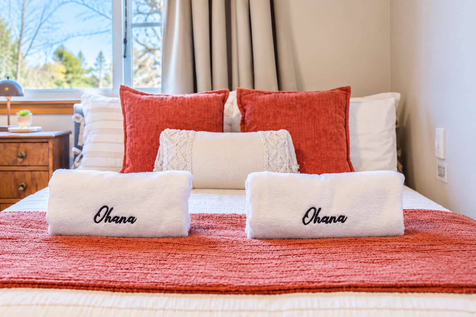 A neatly made bed with two towels labeled 'Ohana' and a red blanket.