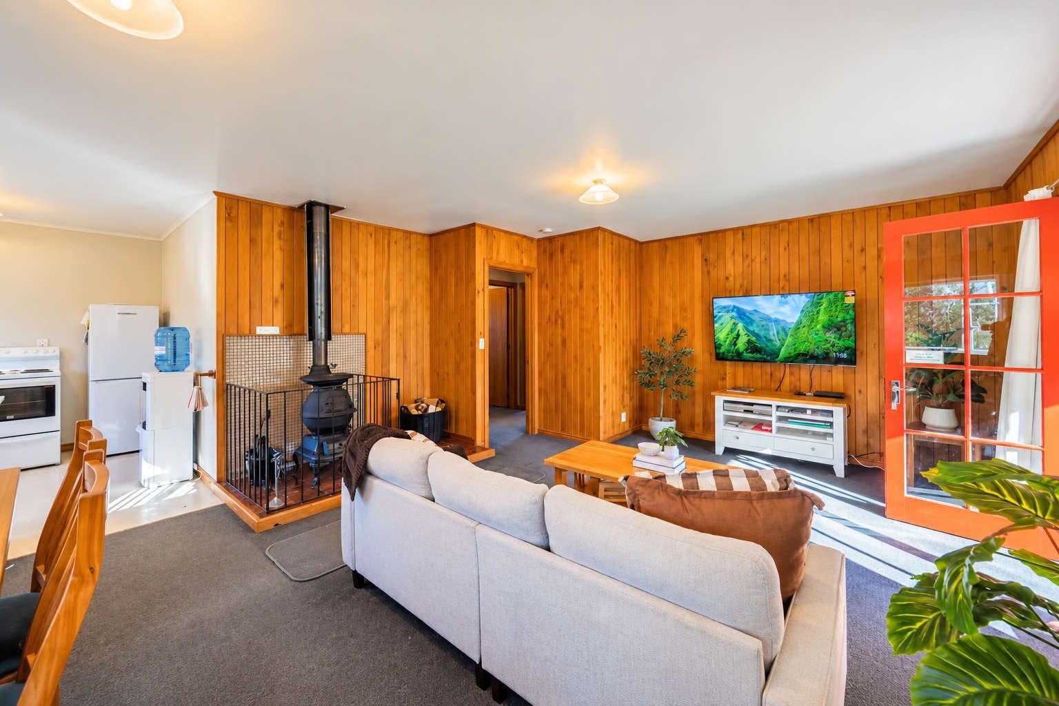 A cozy living room with a sofa, a television, and a kitchen area with a stove and refrigerator.