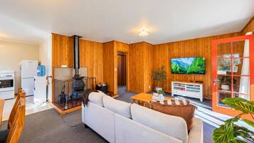 A cozy living room with a sofa, a television, and a kitchen area with a stove and refrigerator.
