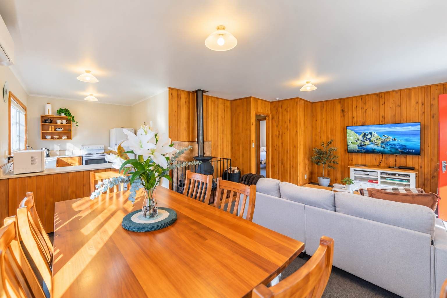 A modern living room with a wooden dining table, a sofa, and a television mounted on the wall.