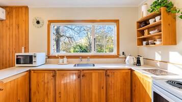 A kitchen with wooden cabinets, a microwave, a sink, and a window with a view of trees.