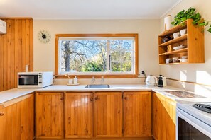 Une cuisine avec des meubles en bois, un four à micro-ondes, un évier et une fenêtre donnant sur les arbres.