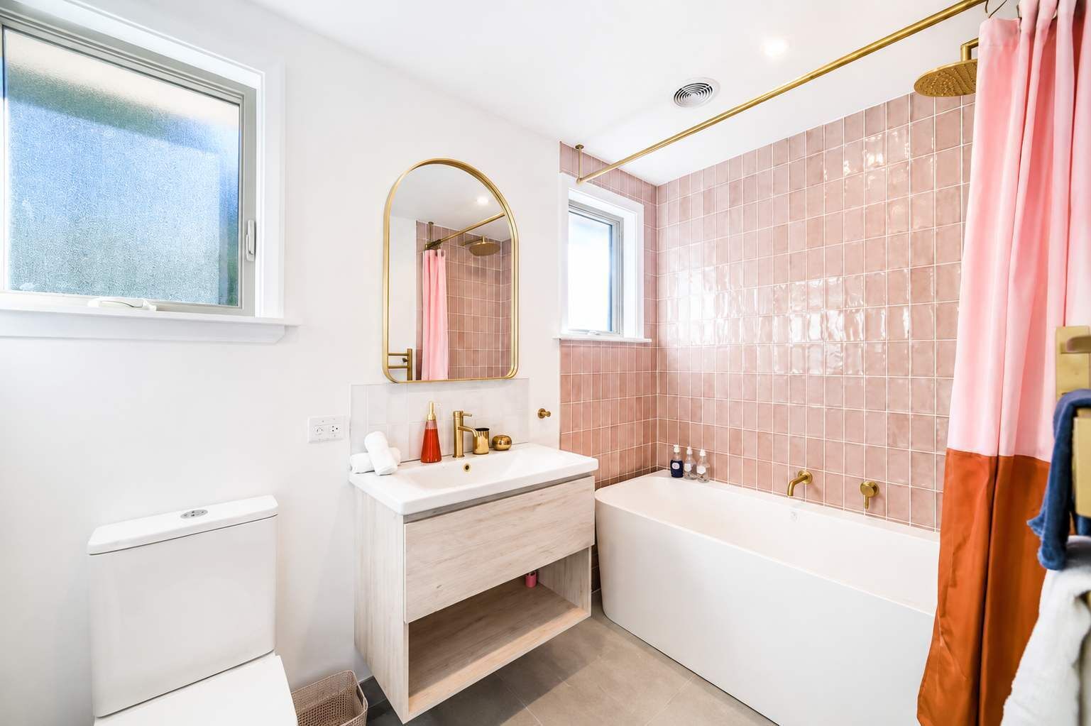 A modern bathroom with a white vanity, a freestanding bathtub, and pink-tiled walls.