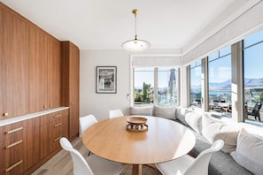 A modern kitchen with a round dining table, white chairs, and a view of the outdoors through large windows.