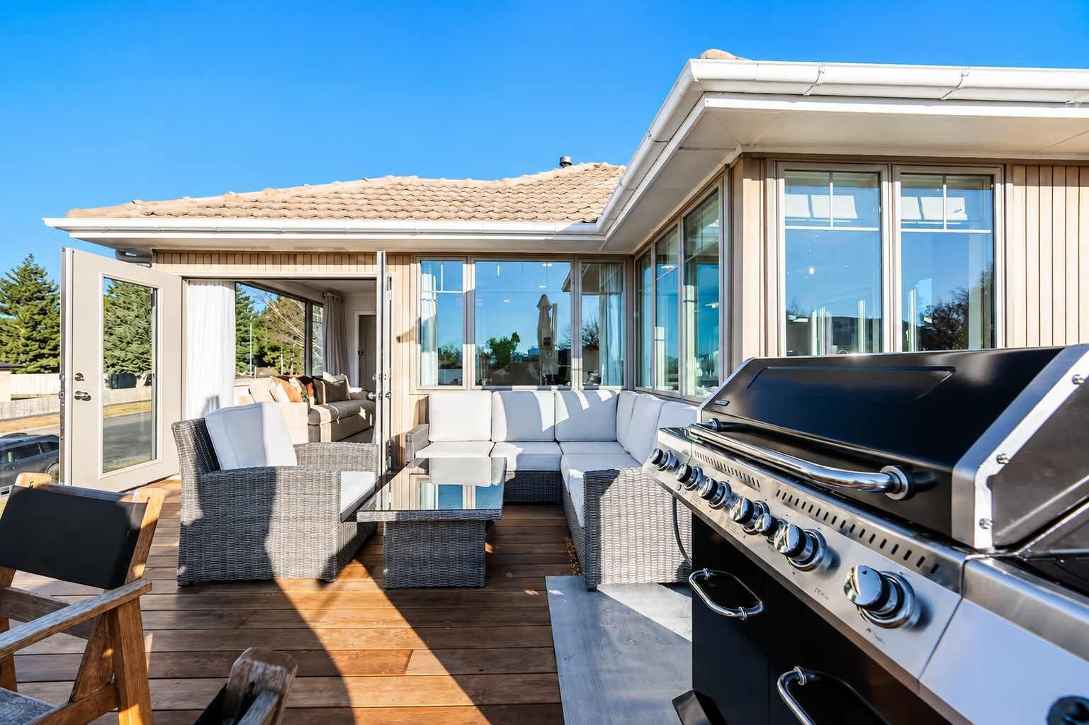 An outdoor deck with a grill, seating area, and glass doors leading to a covered space.