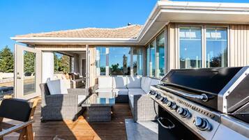 An outdoor deck with a grill, seating area, and glass doors leading to a covered space.