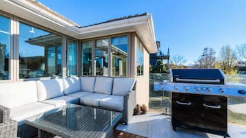 An outdoor deck with a white sofa, a glass-top table, and a built-in grill.