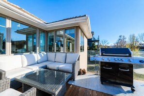 Eine Terrrasse im Freien mit einem weißen Sofa, einem Tisch mit Glasplatte und einem eingebauten Grill.