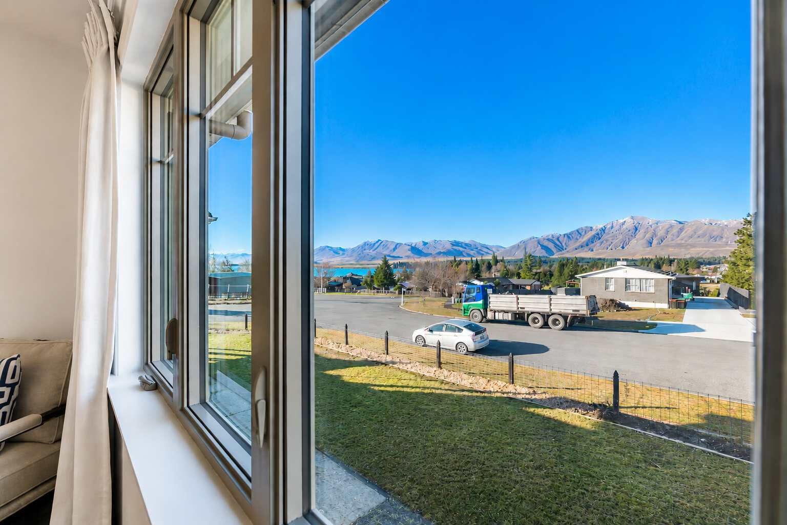 A window view of a parking lot with a mountain backdrop, a truck, and a car.