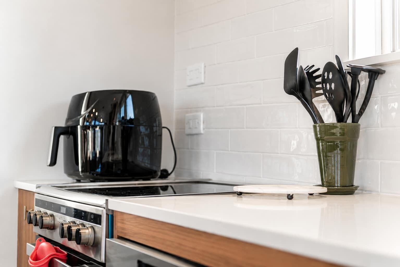 A kitchen with a black coffee maker, a green utensil holder, and a white tiled backsplash.