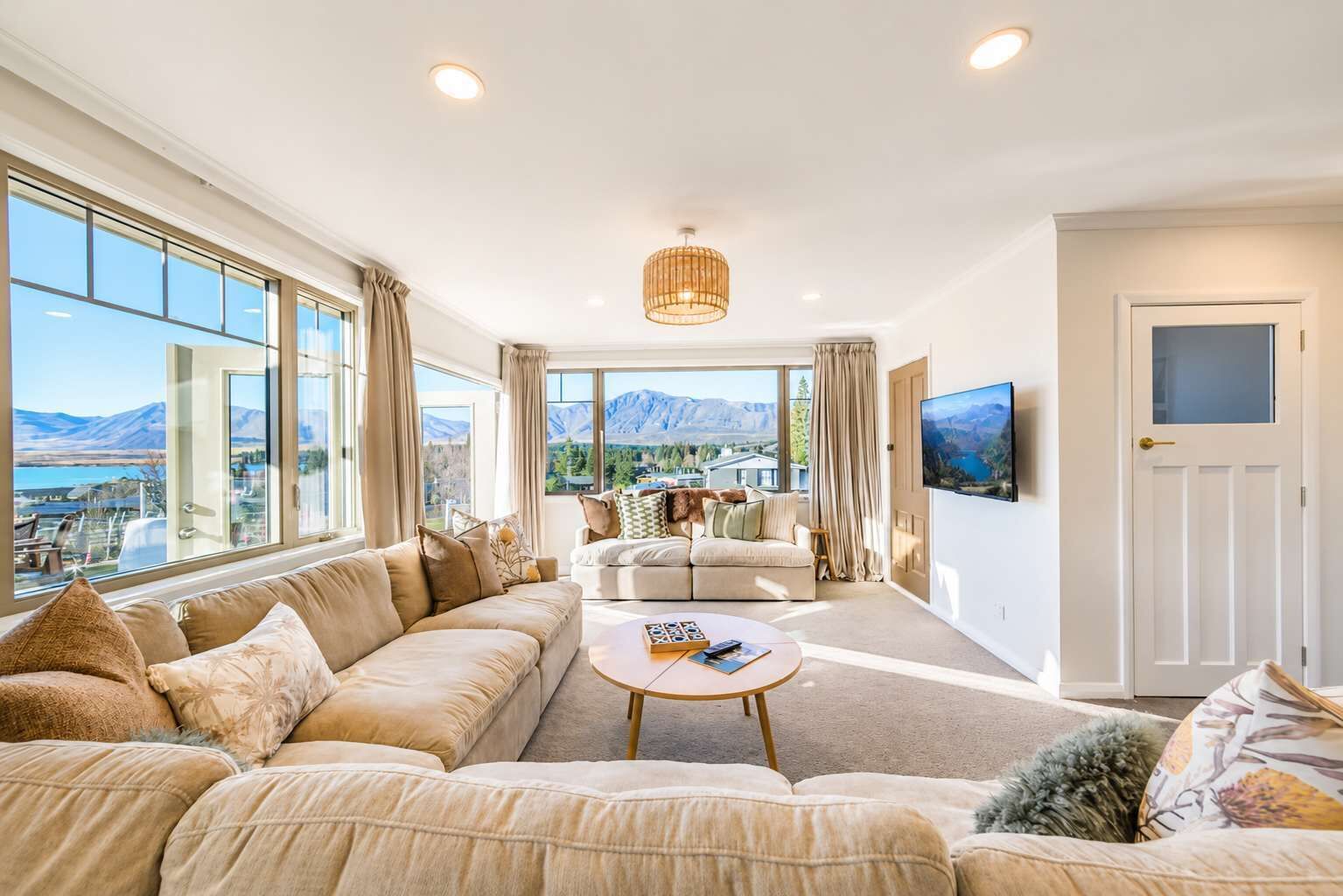 A spacious living room with a large sofa, a coffee table, and a television on the wall.