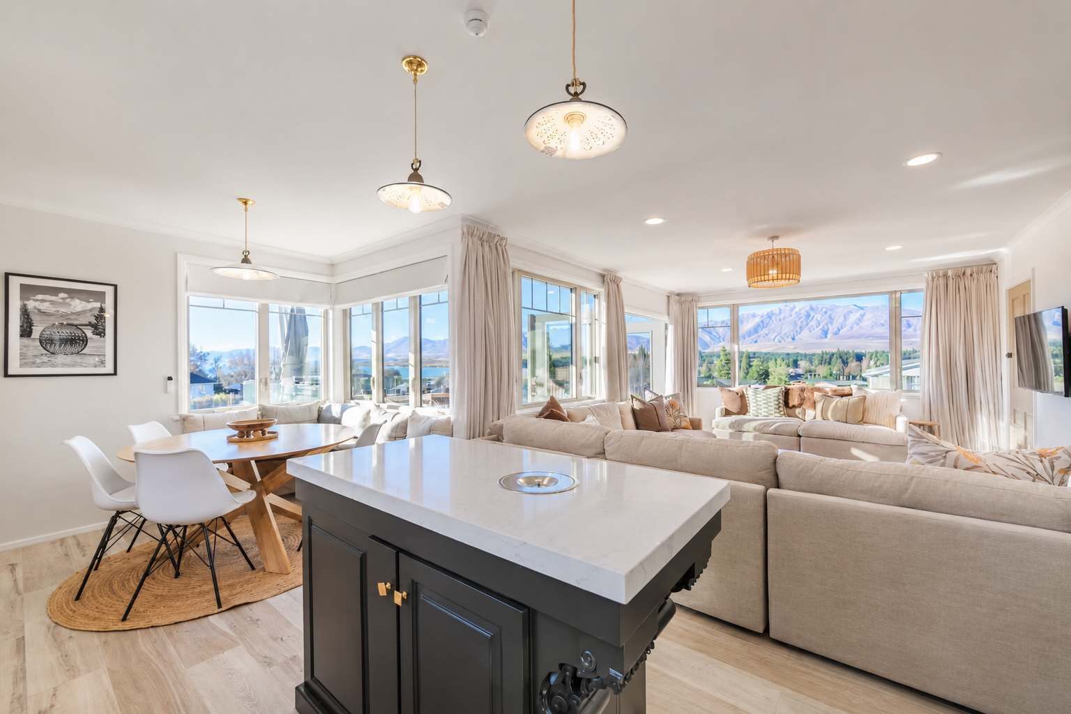 A modern kitchen with a central island, dining area with chairs, and a living area with sofas.