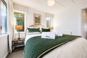 Ein ordentlich eingerichtetes Schlafzimmer mit einem Bett, Kissen, einem Nachttisch, einer Lampe und einem Fenster.