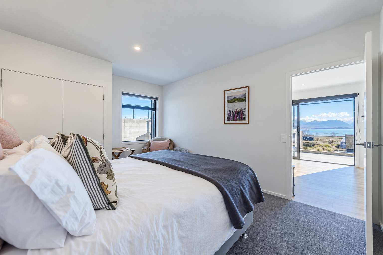 Une chambre à coucher avec un grand lit, un bureau et une vue sur un plan d’eau, visible à travers une porte ouverte.