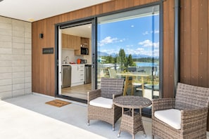 A modern outdoor seating area with wicker furniture and a glass door leading to a kitchen. - The Nook | Lake Views + Private Patio | Tekapo (Lake Tekapo)