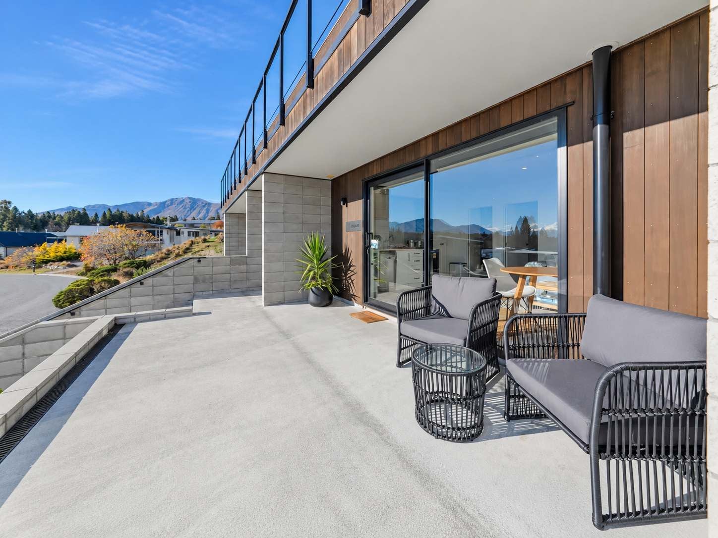 A modern outdoor seating area with a concrete floor, a wooden deck, and a view of a mountain range.