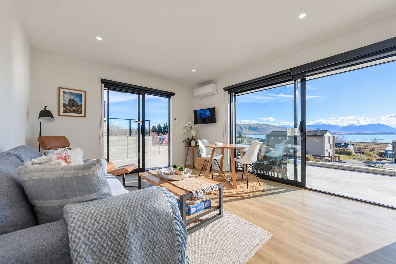 En moderne stue med sofa, sofabord og spiseområde, med store skydedøre til en balkon med en smuk udsigt.