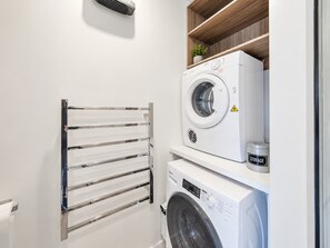 Un cuarto de lavandería con una lavadora de carga frontal, una secadora y un tendedero metálico.