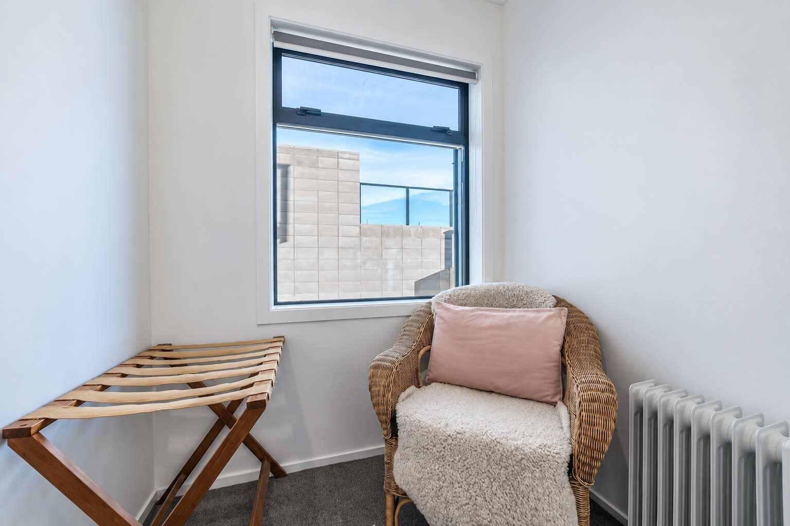 A corner room with a window, a wicker chair with a cushion, and a wooden bench.