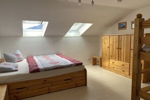 Un dormitorio con cama de madera, dos tragaluces, un armario y una mesita.