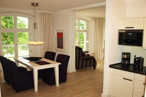 A modern kitchen with a built-in microwave and coffee maker, a dining area with a table and chairs, and large windows with curtains. - Hohen Niendorf Castle (Hohen Niendorf)