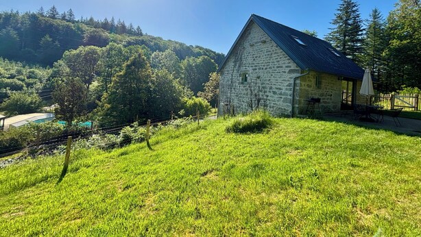 A stone building with a sloped roof, surrounded by lush greenery and trees. - The Gîte de Couturas – Fenced-in garden and shared pool in Corrèze (Saint-Hilaire-les-Courbes)