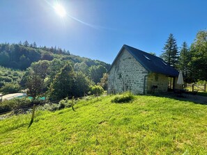 Un bâtiment en pierre doté d’un toit en pente, entouré d’une végétation luxuriante et d’arbres.