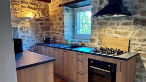 A kitchen with stone walls, a window, a gas stove, and wooden cabinets. - The Gîte de Couturas – Fenced-in garden and shared pool in Corrèze (Saint-Hilaire-les-Courbes)