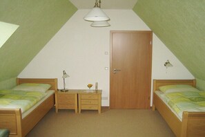 A small, triangular room with two wooden beds, a desk with drawers, a door, and a ceiling light fixture. - Sonnenblick Apartment (Schwielochsee)