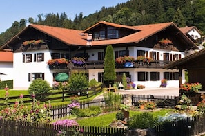 A traditional chalet with a sloped roof, wooden balconies with flower boxes, and a well-maintained garden with a wooden fence. - Cellar - Castle view (Hopfen am See)