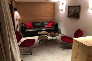Ein gemütliches Zimmer mit einem schwarzen Ledersofa, roten Kissen und zwei kleinen Holztischen.