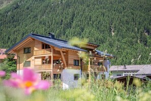 Eine zweistöckige Holzhütte mit Balkonen, eingebettet in eine bewaldete Berglandschaft.