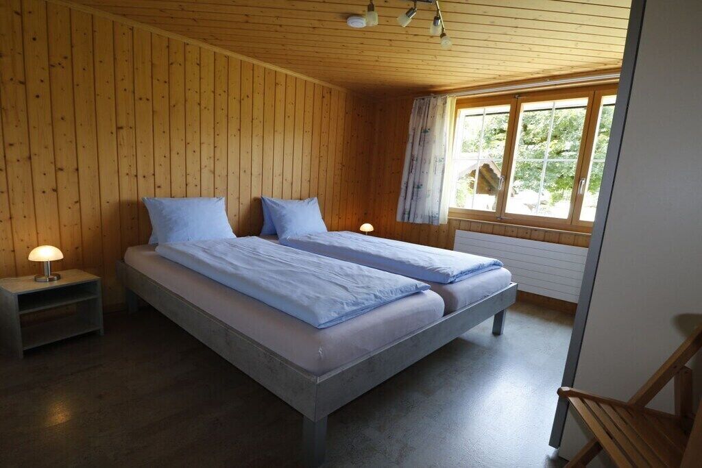 Une chambre avec deux lits, des murs en bois, une fenêtre donnant sur un beau paysage et une table de chevet avec une lampe.